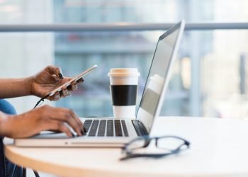 hands typing on laptop while holding mobile phone