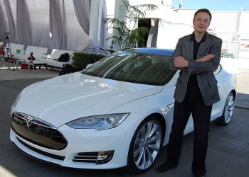A younger Elon Musk in front of a white Tesla
