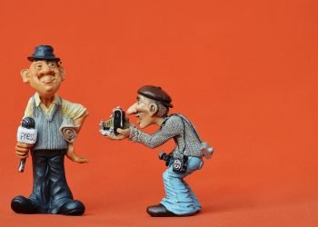Two model caricature male figures wearing hats, one has many cameras and one has a microphone with the word Press on it