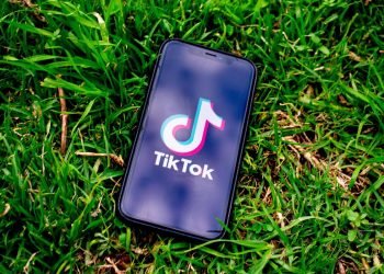 A mobile phone lies on the grass with its screen set to the TikTok home page