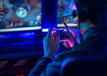 Close-up, video game console controller in gamer hands at colorful neon light living room at night, E-sport streaming game online.