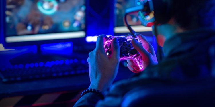 Close-up, video game console controller in gamer hands at colorful neon light living room at night, E-sport streaming game online.