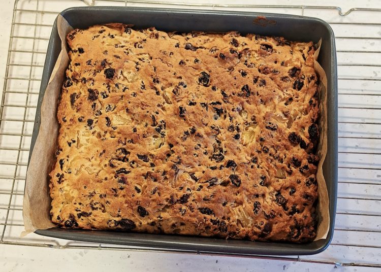 A fruit cake cools in a baking tin on a rack