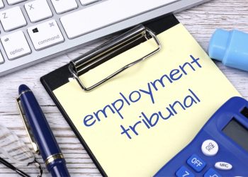 A desk with calculator, keyboard, pens and spectacles surrounding a clipboard with the words Employment Tribunal written on it
