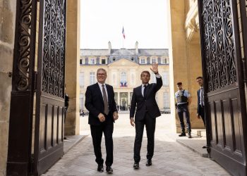 Keir Starmer and Emmanuel Macron who has his arm raised stand in a grand doorway