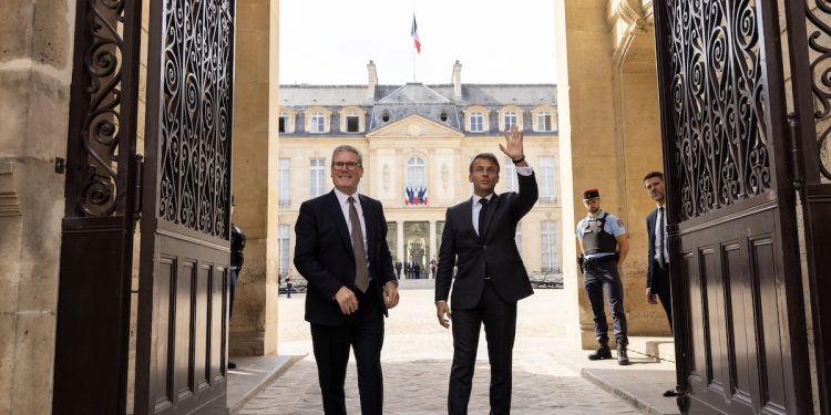 Keir Starmer and Emmanuel Macron who has his arm raised stand in a grand doorway