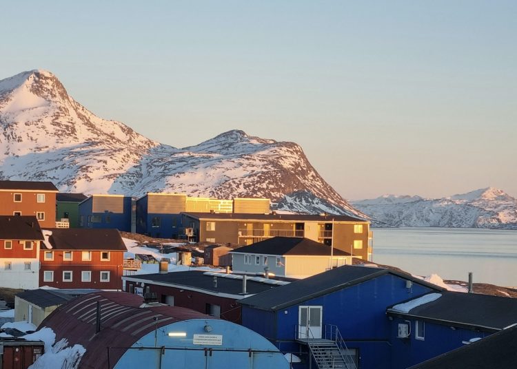 sun over a small group of houses against ice covered mountains and sea