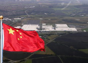 an aerial view of a large white factory building which is the Sunderland car plant for Nissan and a Chinese flag superimposed