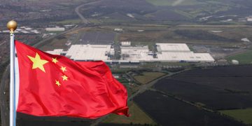 an aerial view of a large white factory building which is the Sunderland car plant for Nissan and a Chinese flag superimposed