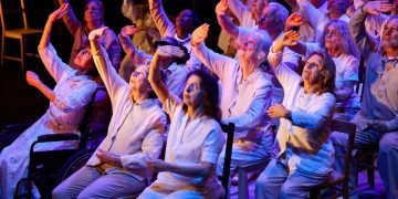 older people sitting on chairs holding their right arms above their heads as if to shield themselves