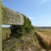 a wooden waymark sign reading Yorkshire Wolds Way points down along a track by the side of a field of crops