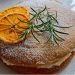 a sponge cake dusted with icing sugar and decorated with orange slices and rosemary stalks