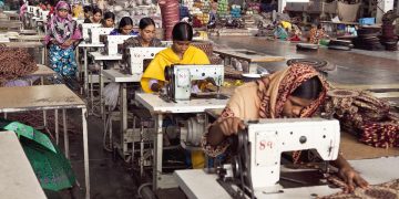 rows of Asian women sit at sewing machines in a factory
